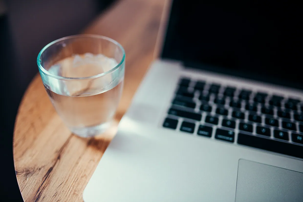 A clear glass of water sits next to a laptop