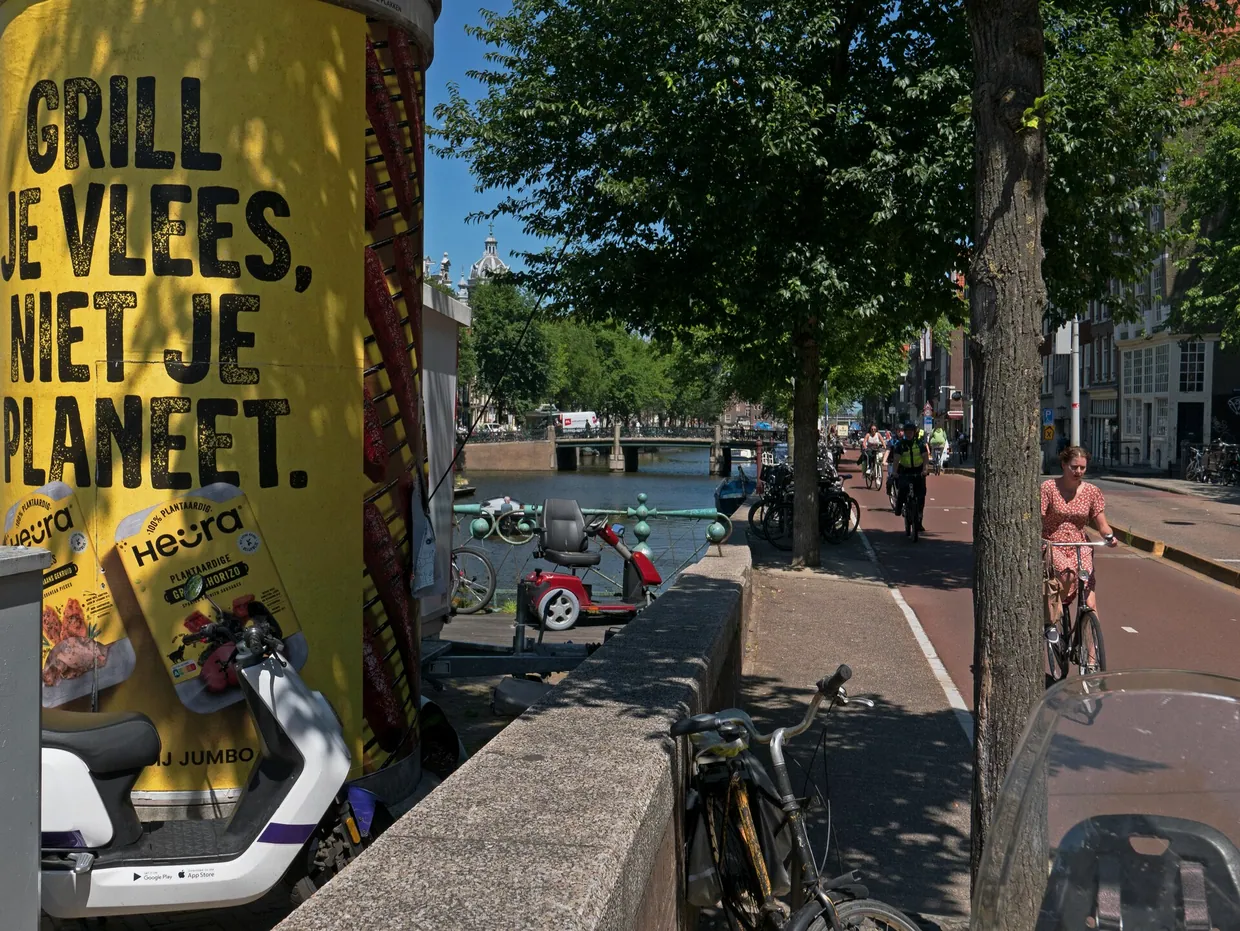 A street view over the Geldersekade canal and bike path in downtown Amsterdam, with a large billboard; free photo Amsterdam city, Fons Heijnsbroek July 2022