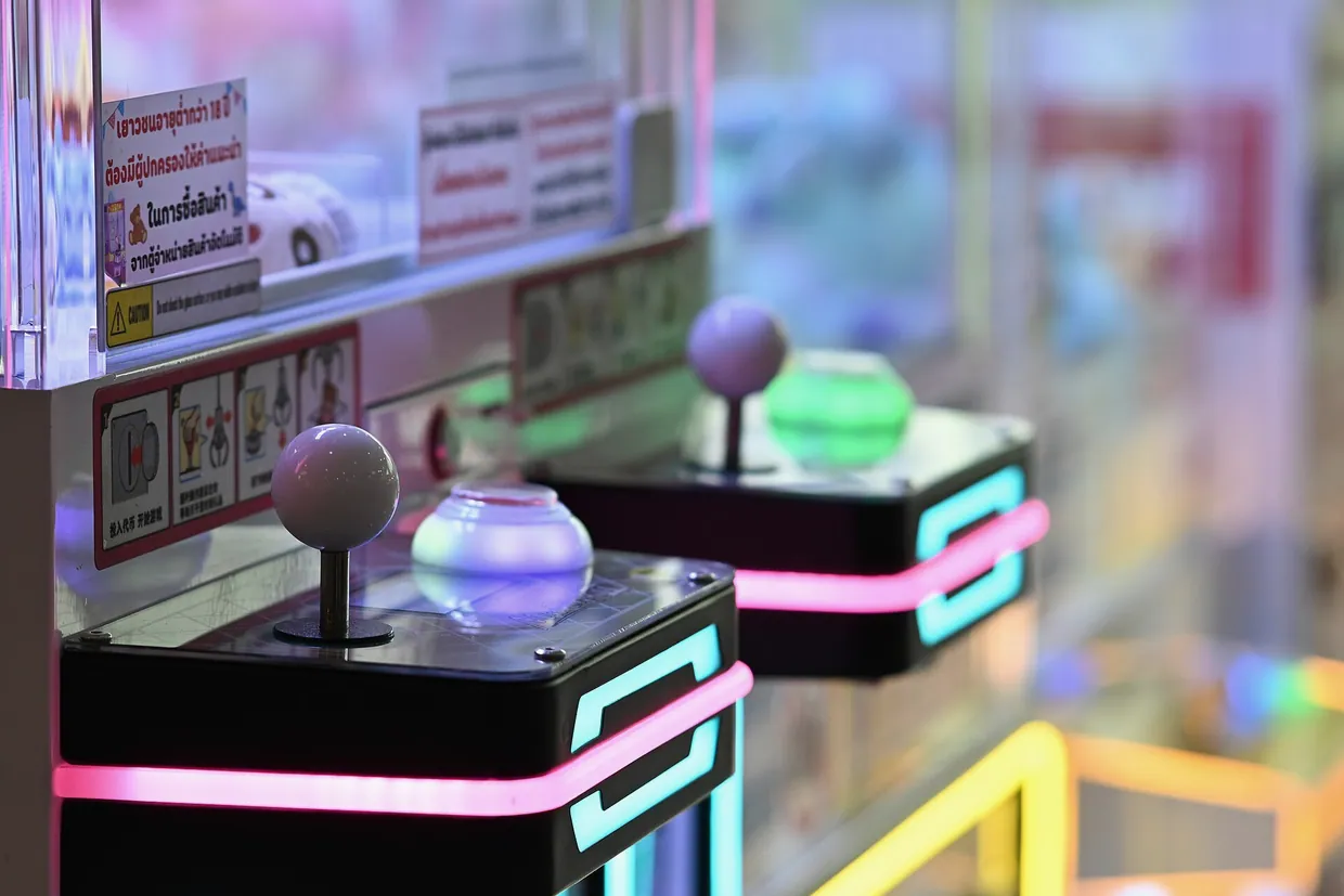 DFC 0798 Close-up of illuminated arcade claw machines with glowing joysticks and neon accents