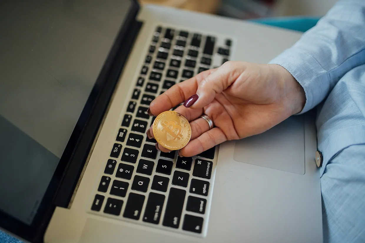 Close-up of a Bitcoin physical coin in a womans hand and a laptop on her lap